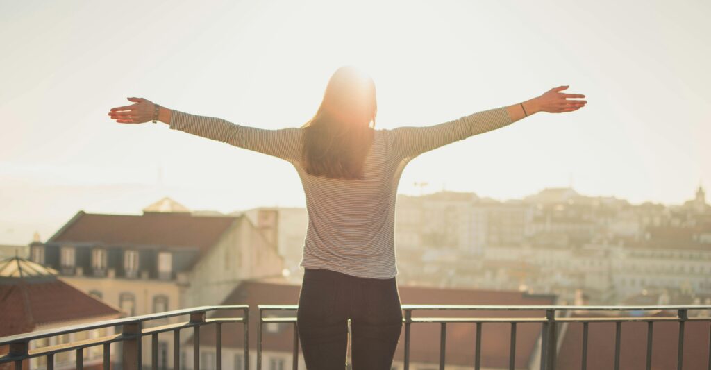 Une femme qui se tient debout les bras ouverts face à la lumière du matin. Sensation d'harmonie et d'équilibre